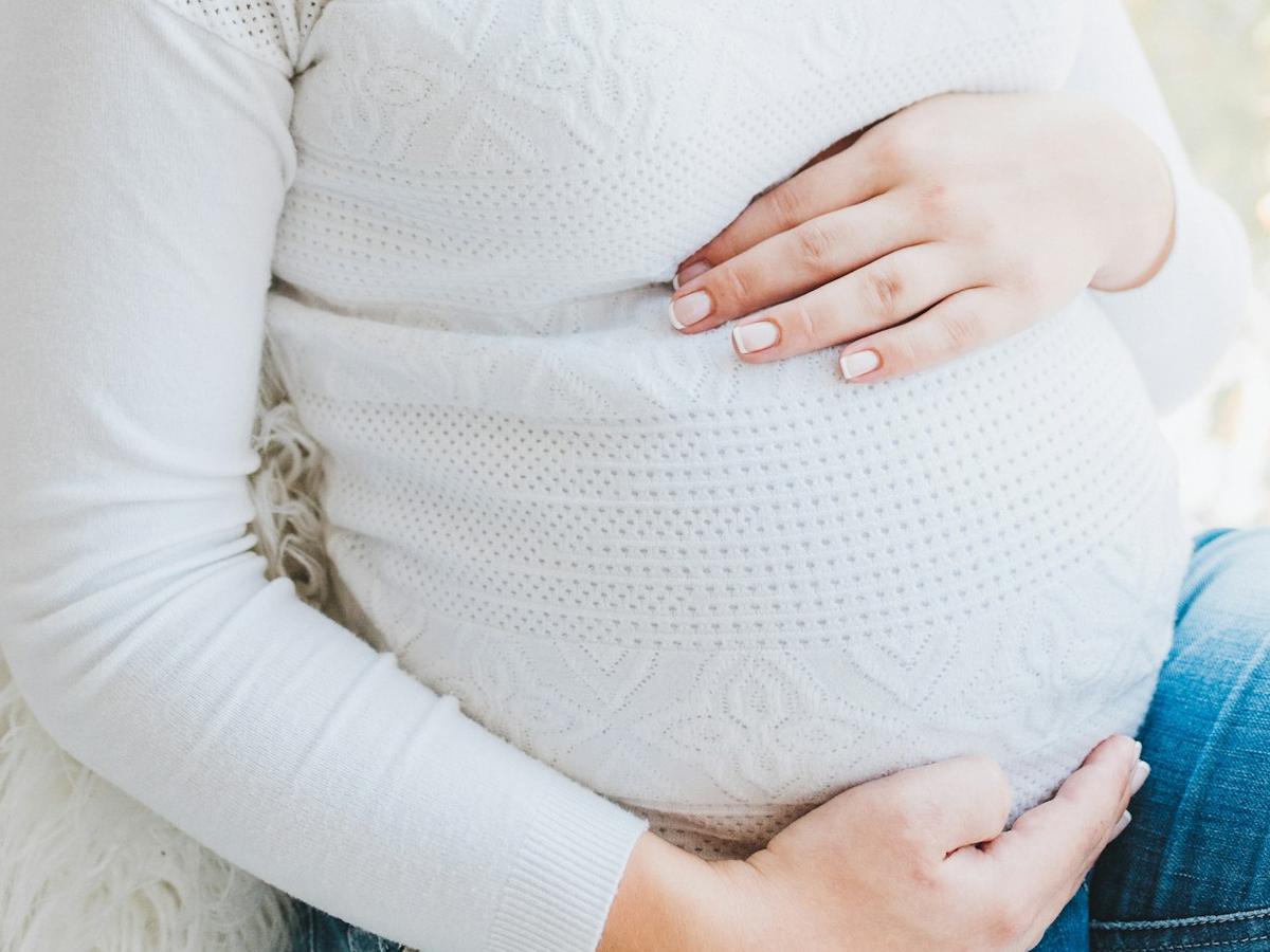 Pregnant woman in a white jumper with her hands on her bump